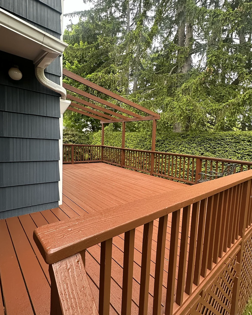 Freshly stained deck with matching railings, lattice skirting and a wood pergola against blue-gray shingle siding