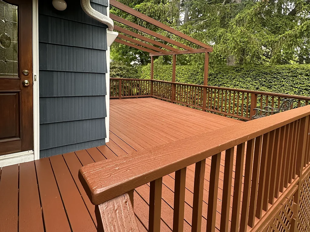 Freshly stained deck with matching railings, lattice skirting and a wood pergola against blue-gray shingle siding