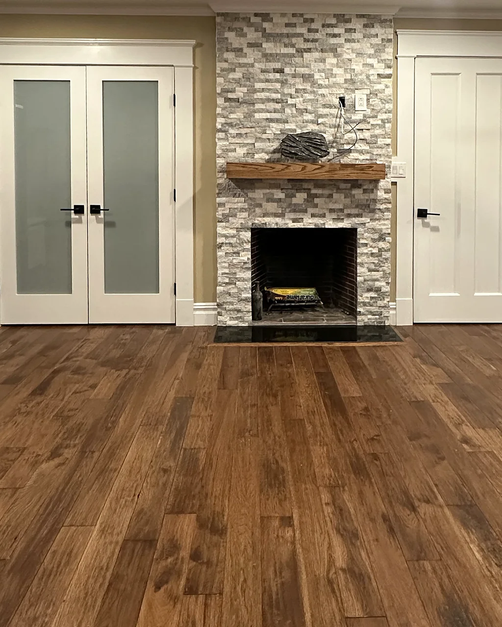 Stacked-stone fireplace with a wood mantel between white French doors, over hand-scraped hardwood floors