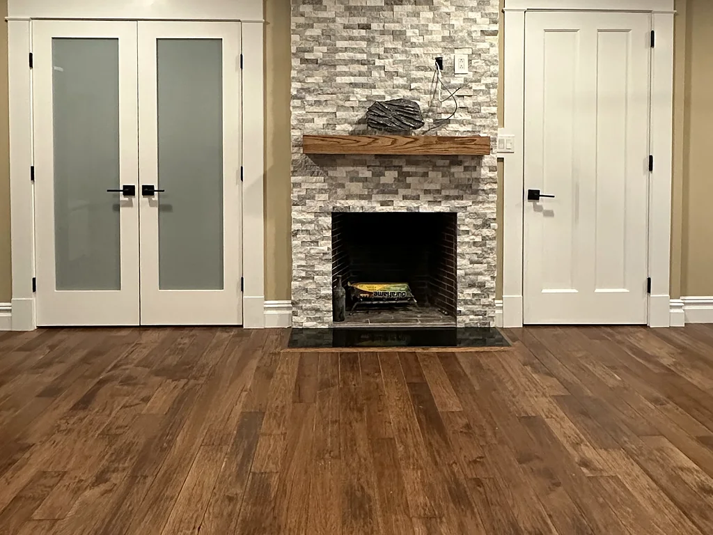 Hand-scraped hardwood floors in front of a stacked-stone fireplace and white French doors