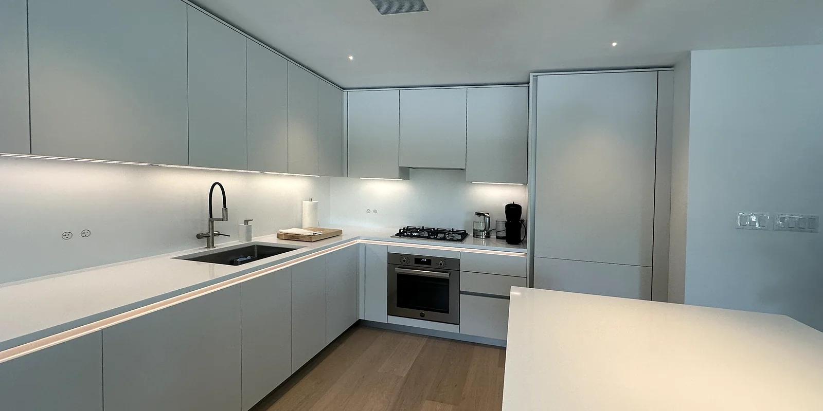 Modern white kitchen with handle-free cabinets, under-cabinet lighting, a gas cooktop and a quartz island