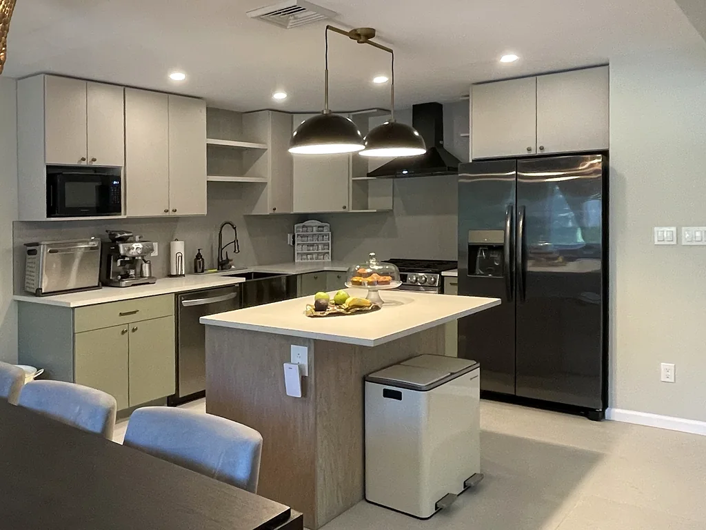 Renovated kitchen with sage green lower cabinets, light gray uppers, an island and black pendant lights