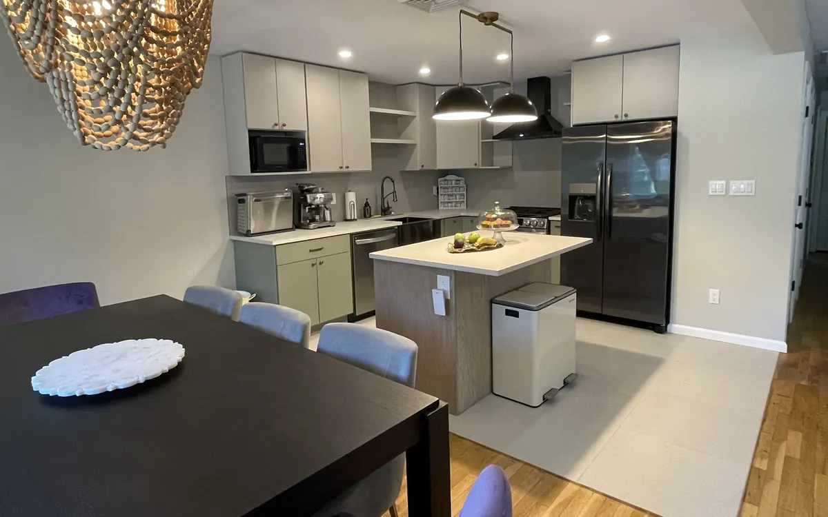 Renovated kitchen with sage green lower cabinets, light gray uppers, an island and black pendant lights